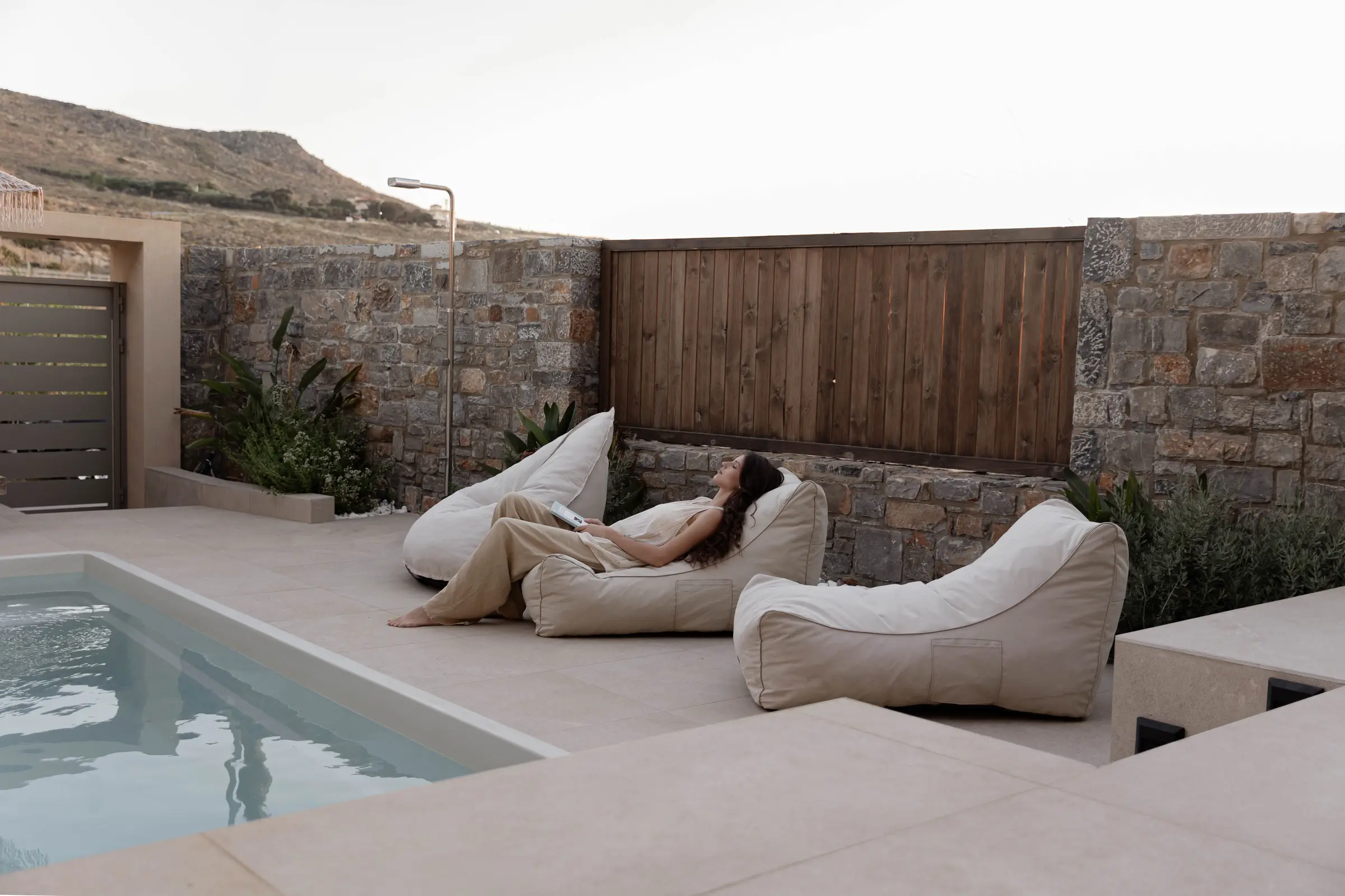 Guest relaxing on beanbag loungers beside the Deluxe Suite pool at dusk, hillside beyond