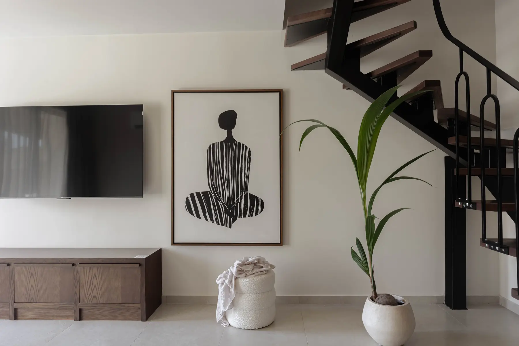 Framed artwork and palm beneath the black steel staircase